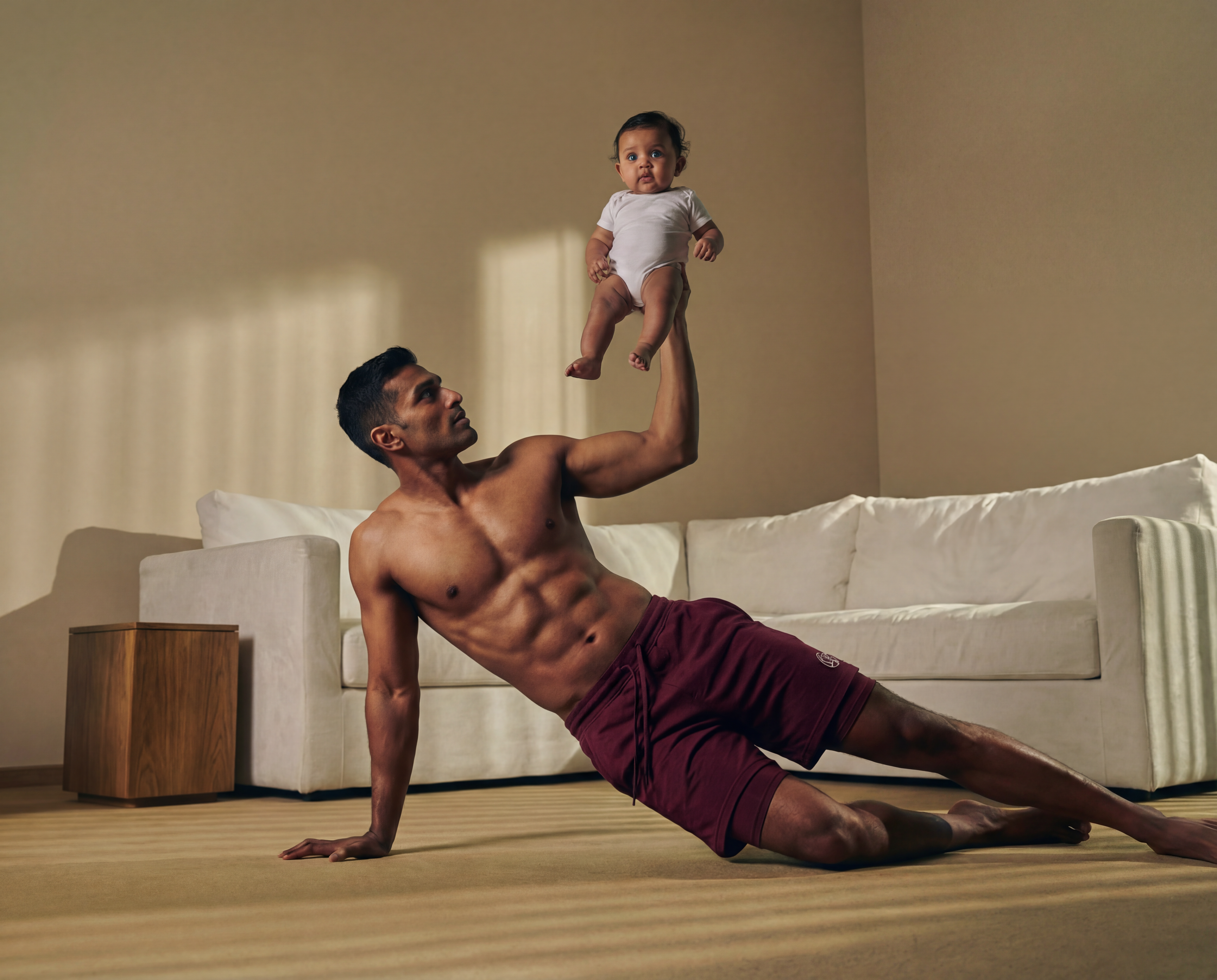 Man in a plank position holding a baby in a living room.
